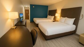 A hotel room with two beds, a desk, a chair, and a TV.