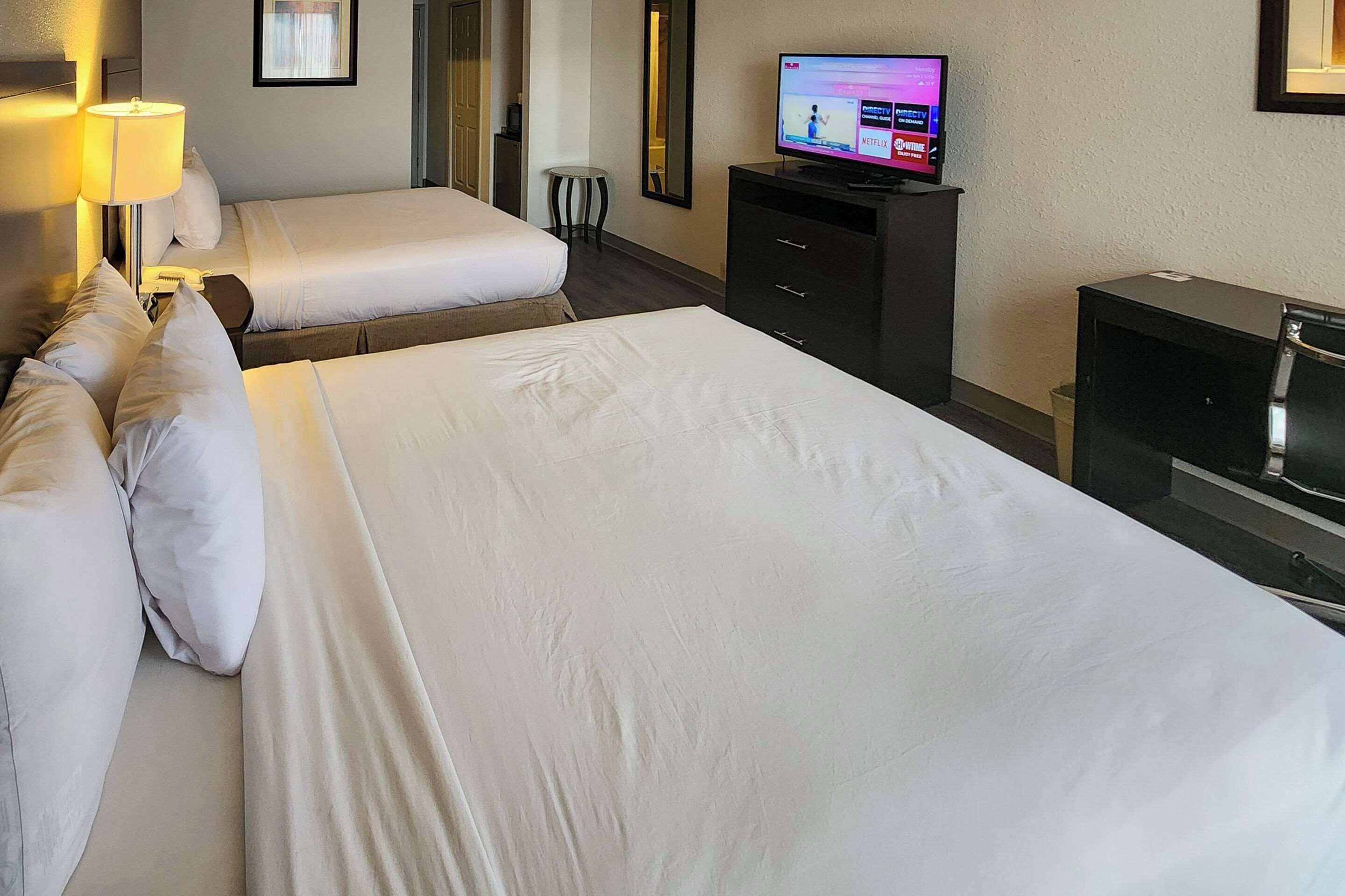 A hotel room with two beds, a TV, a desk, and a lamp.