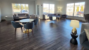 A spacious room with a large window, a sofa, a round table, and several chairs.