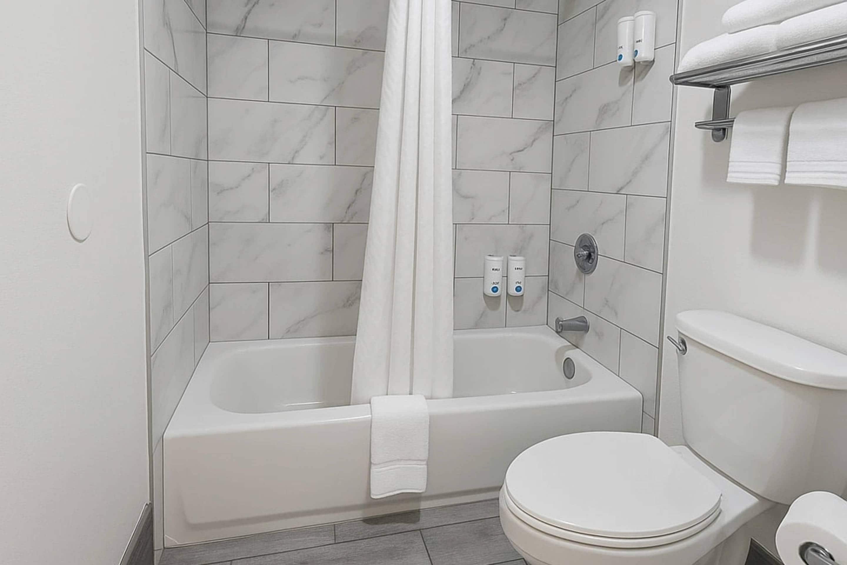 Un baño con bañera, inodoro y azulejos de mármol.