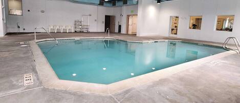 Una piscina interior con agua cristalina, rodeada de un suelo de baldosas y paredes blancas.