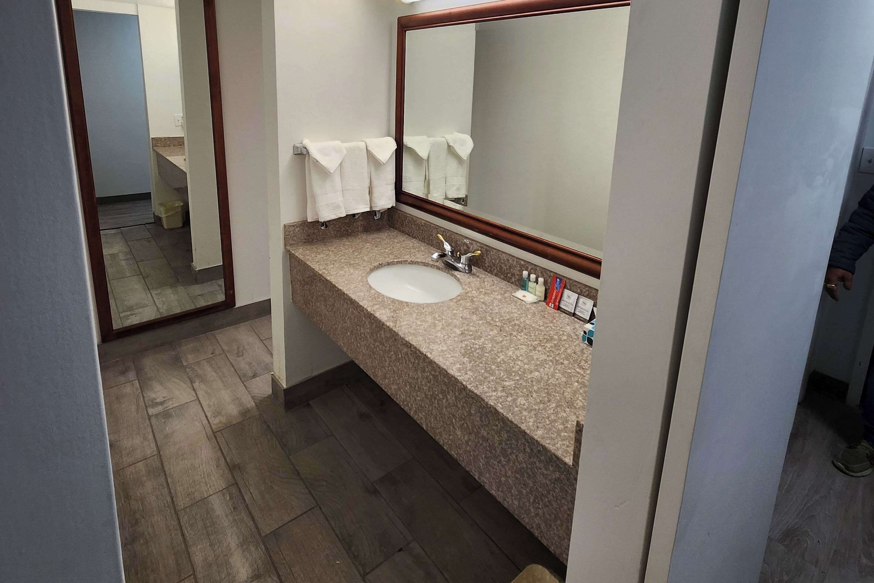 Une salle de bain avec un comptoir en granit, un lavabo, un miroir et deux serviettes blanches accrochées au mur.
