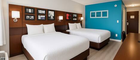 Habitación de hotel con dos camas, cabecero de madera, pared azul decorativa y un escritorio de madera.