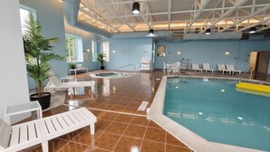 An indoor swimming pool with clear water, surrounded by white lounge chairs and a potted plant.