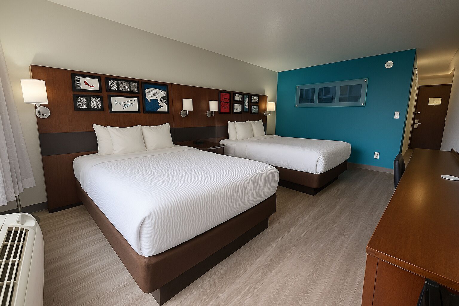 A hotel room with two beds, a wooden headboard, wall art, and a desk.