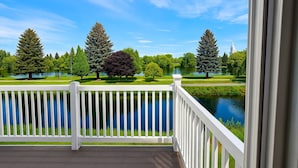 A wooden deck with a white railing overlooking a lake and trees.