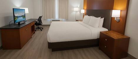 Une chambre d’hôtel avec un grand lit, un bureau avec un ordinateur, une chaise, deux lampes de chevet et une fenêtre avec des rideaux.