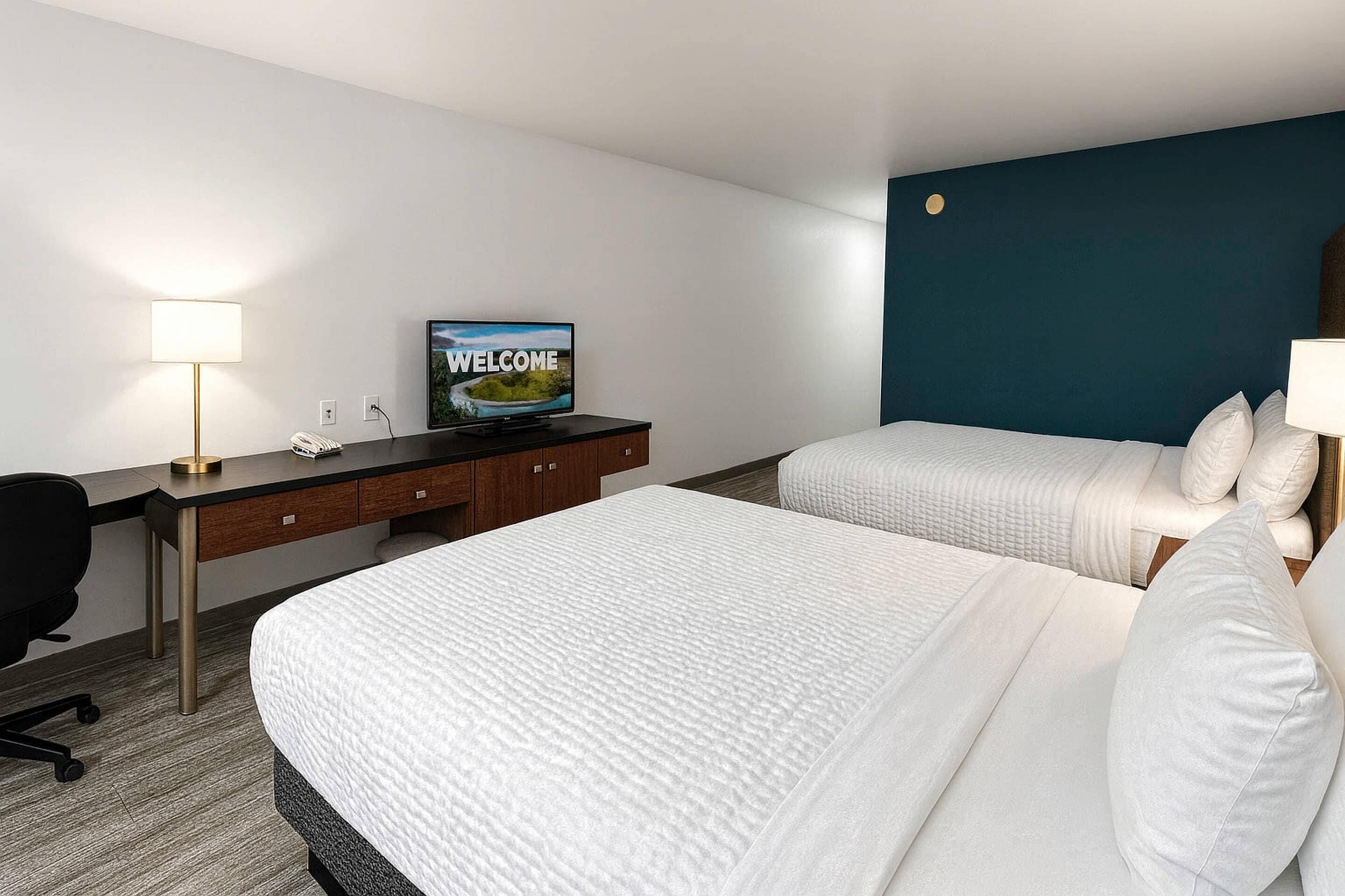 A hotel room with two beds, a desk, a television, and a lamp.