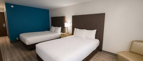 Une chambre d’hôtel avec deux lits, une table de chevet, une lampe et un fauteuil de couleur beige.