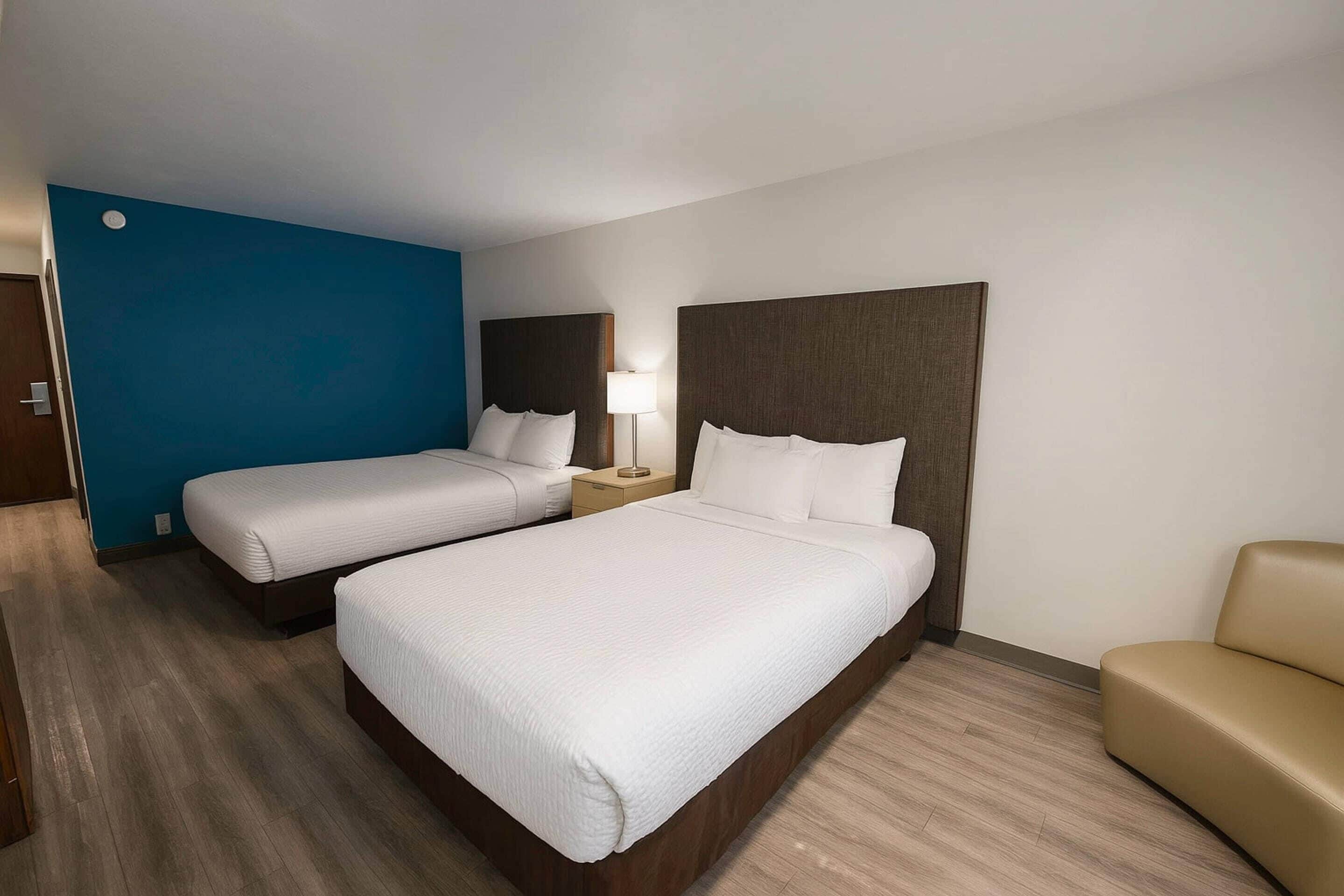 A hotel room with two beds, a sofa, and a nightstand with a lamp.