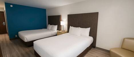 A hotel room with two beds, a sofa, and a nightstand with a lamp.