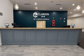 Ein Empfangstresen mit blauer Wand, dem Logo von Clarion Inn by Choice Hotels, zwei Computermonitoren und einem Rauchmelder.