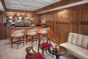 A bar area with a wooden bar counter, multiple liquor bottles, and a sign reading 'TRON SIDE'. There are three bar stools and a sofa in the seating area. - Portland Regency Hotel & Spa (Portland)