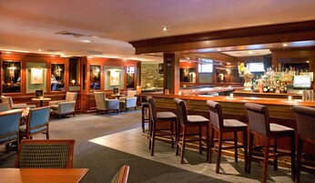 A bar area with multiple seating options, including bar stools and chairs, and a bar counter with a variety of bottles and glasses.