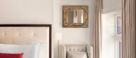 A neatly arranged hotel room with a bed, a chair, a lamp, and a window with curtains.