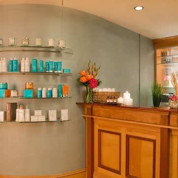 A reception area with a wooden counter, shelves with various products, and a decorative vase with flowers.