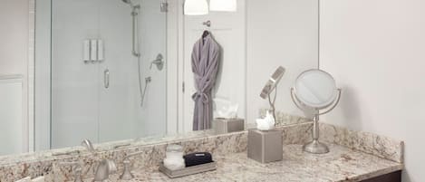 Ein Badezimmer mit einem großen Spiegel, einem Waschbecken, einer Dusche und einem Bademantel, der an der Tür hängt.