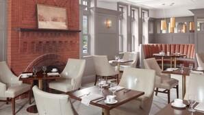 Een restaurant met een open haard van baksteen, witte stoelen en gedekte tafels.