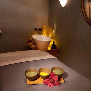 A spa room with a bed, a large basin, and three bowls of bath products.