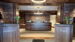 Een receptiegedeelte met twee houten balies, respectievelijk aangeduid met 'eighteen95 restaurant' en 'Valet'.