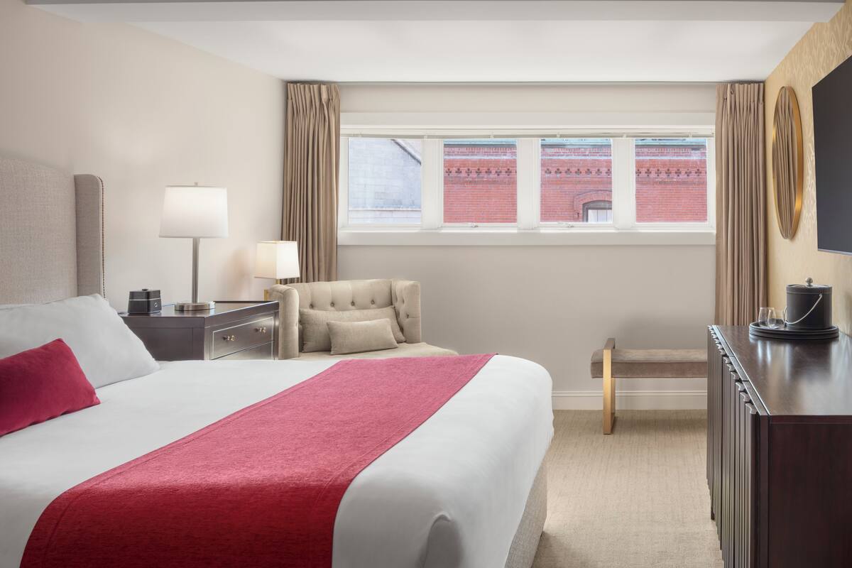 Habitación de hotel con una cama grande, un escritorio con lámpara, una silla, un televisor y una ventana con cortinas.