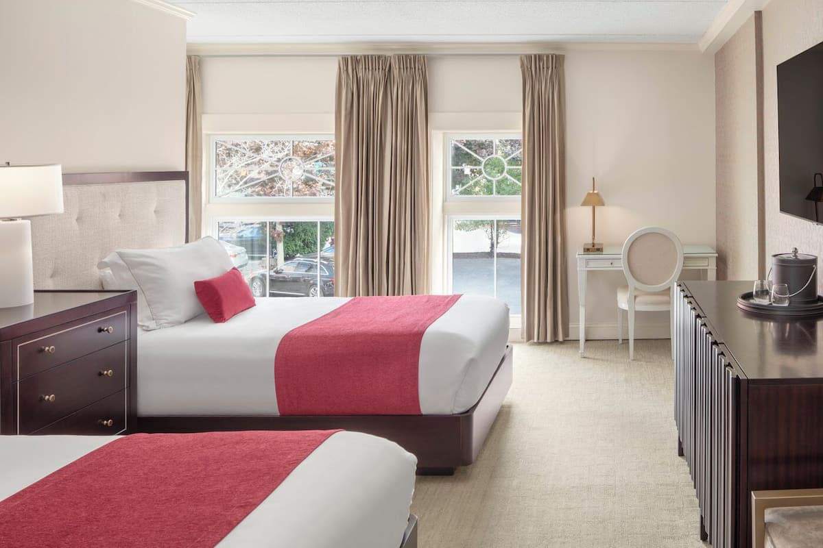 Habitación de hotel con dos camas, un escritorio, una silla, un televisor y vista al exterior.
