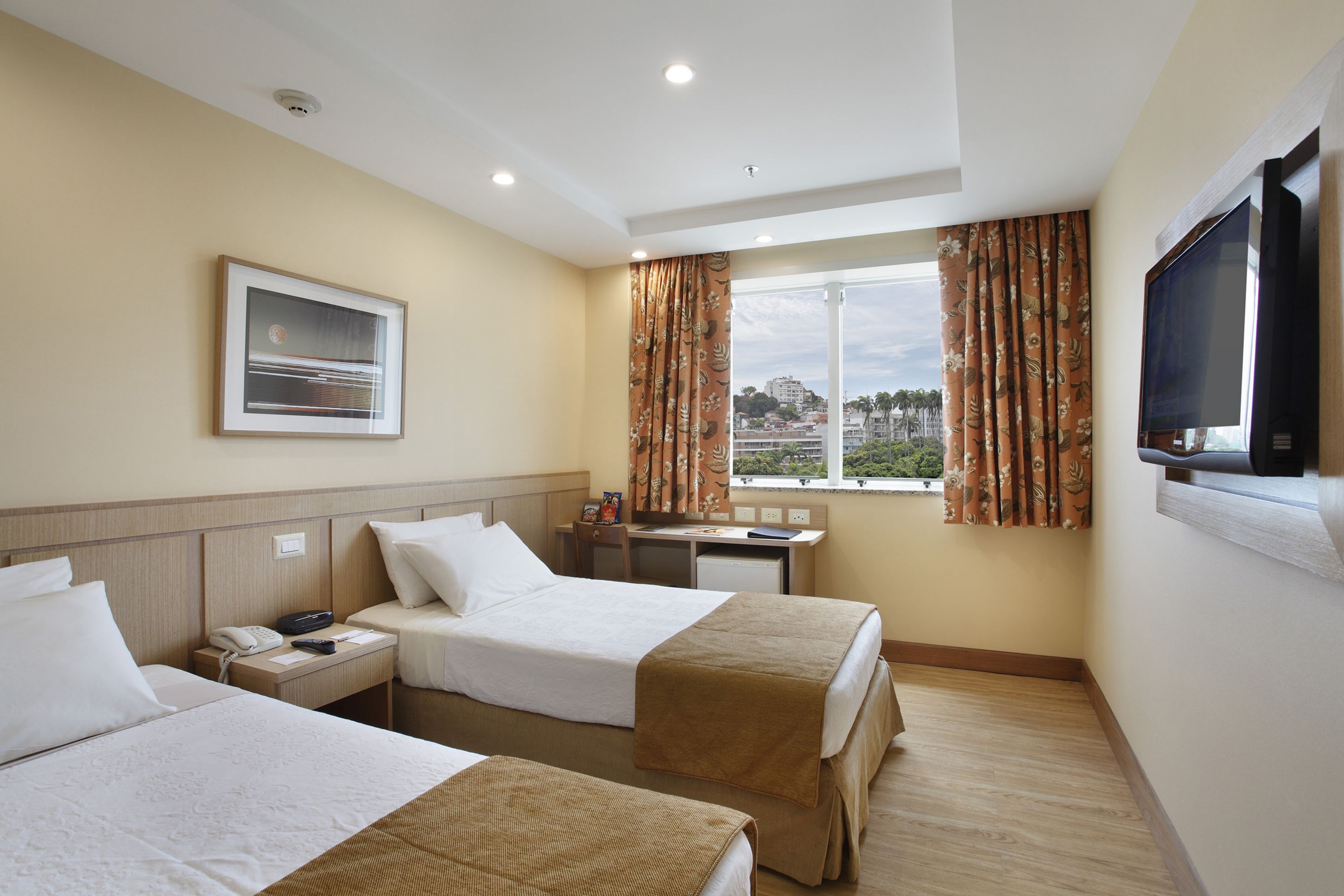 A hotel room with two beds, a desk, a television, and a window with curtains.