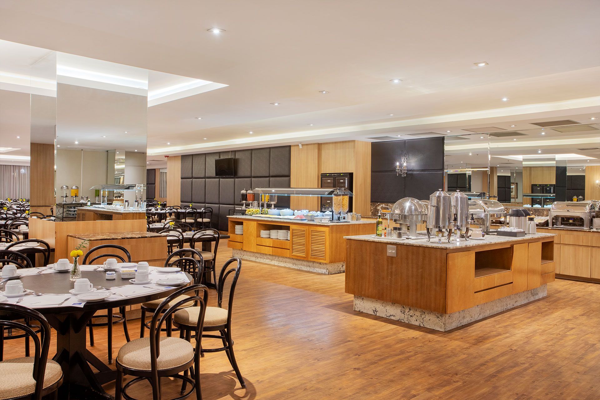 Un comedor de hotel moderno con diversas opciones de asientos, una estación de buffet y una zona de cocina.