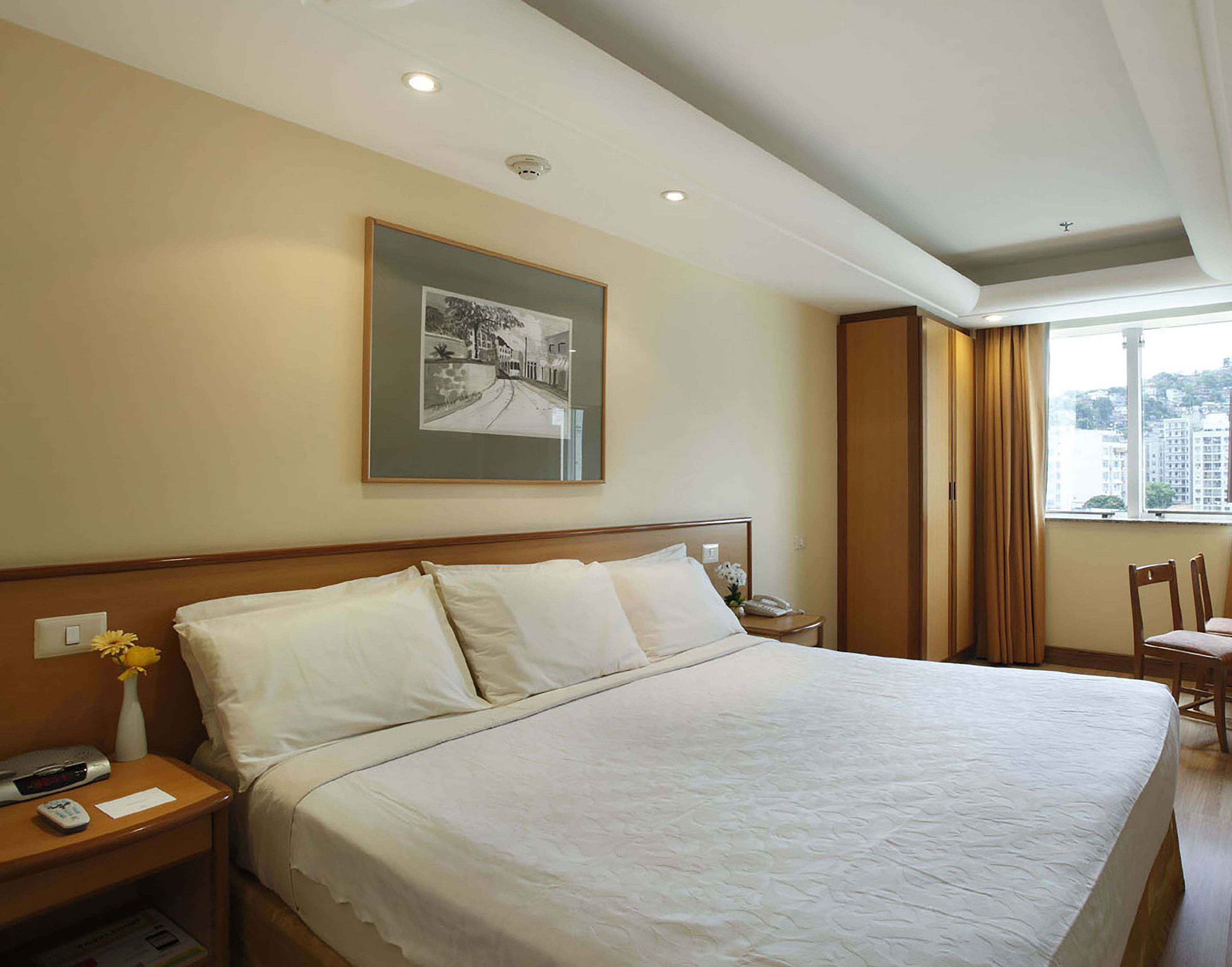 A hotel room with a large bed, a nightstand, a framed picture on the wall, and a window with curtains.