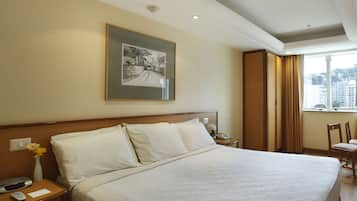 A hotel room with a large bed, a nightstand, a framed picture on the wall, and a window with curtains.