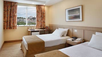 Habitación de hotel con dos camas, un escritorio, una silla, una ventana con cortinas, un cuadro en la pared y un teléfono en la mesita de noche.