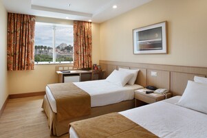 Habitación de hotel con dos camas, un escritorio, una silla, una ventana con cortinas, un cuadro en la pared y un teléfono en la mesita de noche.