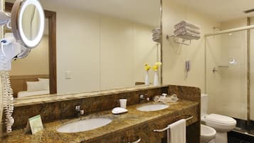 Un baño con dos lavamanos, un espejo grande, cabina de ducha de cristal y un inodoro.