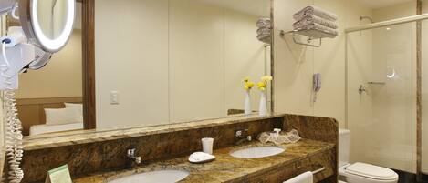 Un baño con dos lavamanos, un espejo grande, cabina de ducha de cristal y un inodoro.