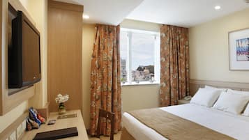 Een hotelkamer met een bed, een bureau met stoel, een televisie en een raam met gordijnen.