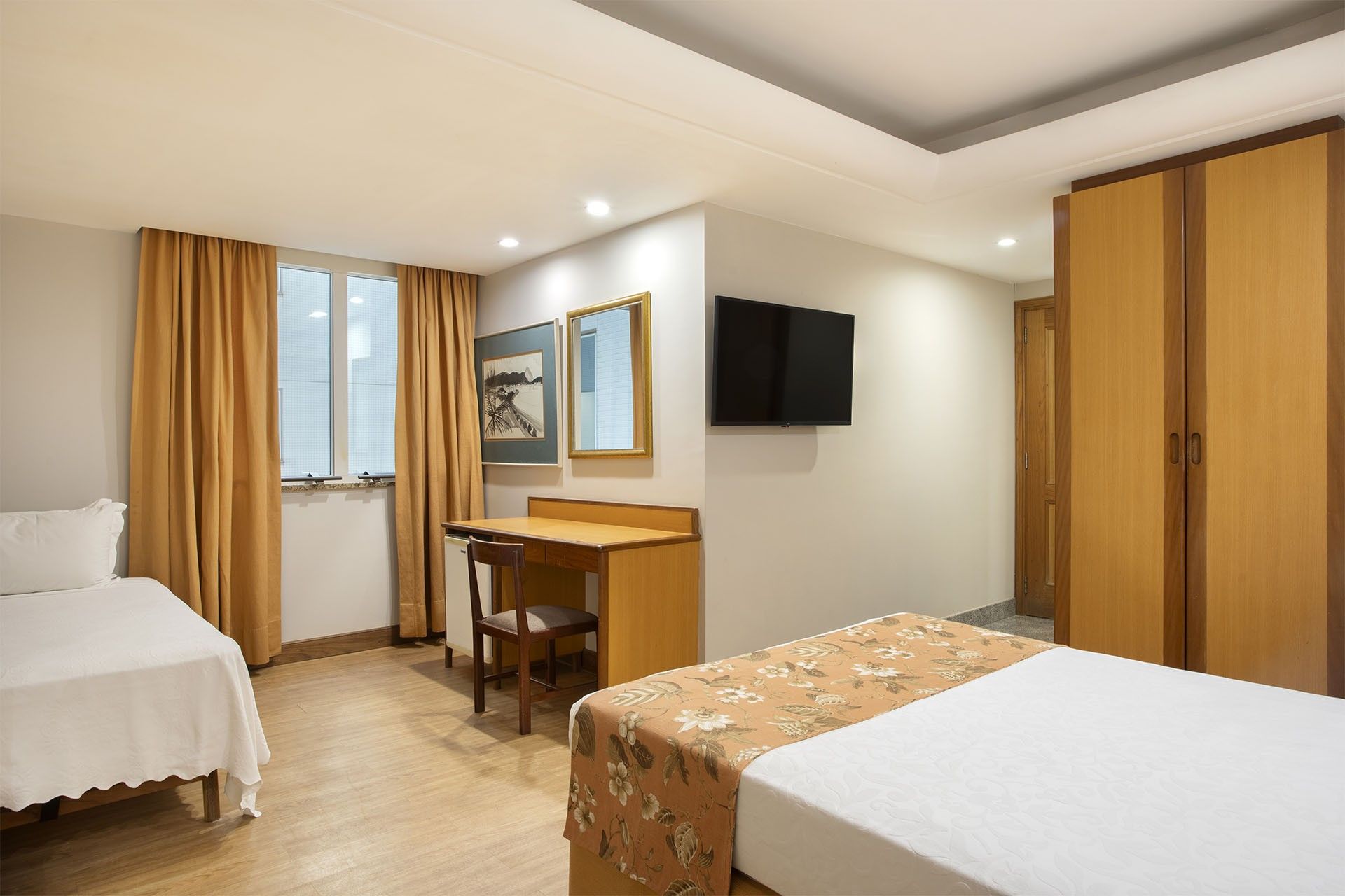 Una habitación de hotel con dos camas, un escritorio, una silla, un televisor y un armario.