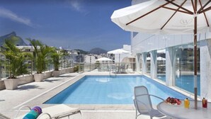 A rooftop pool with clear blue water, surrounded by lounge chairs and umbrellas, overlooking a cityscape with buildings and a mountain. - Windsor Florida Hotel (Rio de Janeiro)