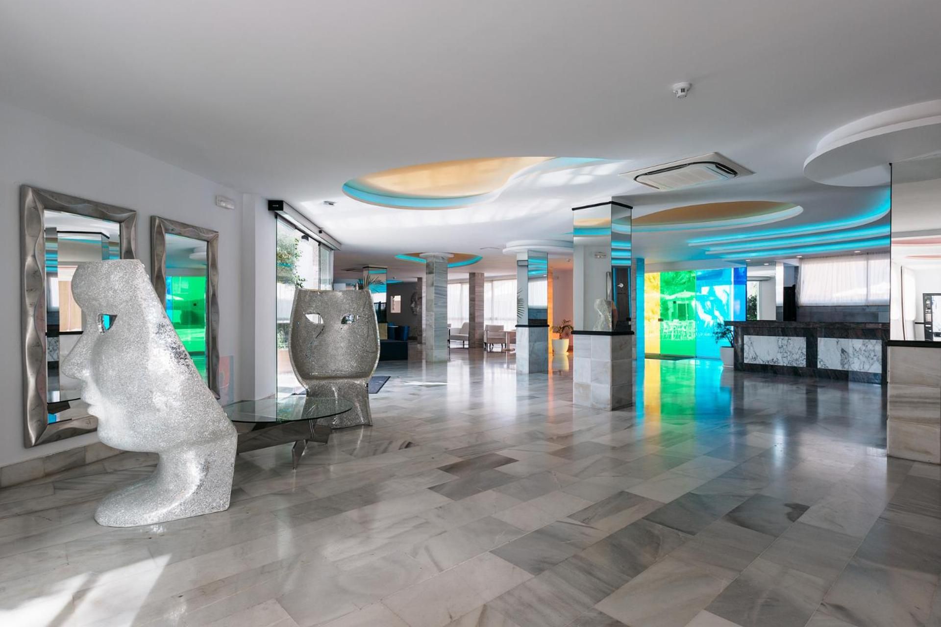 Un vestíbulo moderno con suelo de mármol, esculturas abstractas y una zona de recepción con pantalla digital.