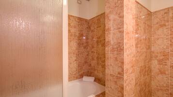 Un baño con una bañera blanca, baldosas color beige y una zona de ducha visible.