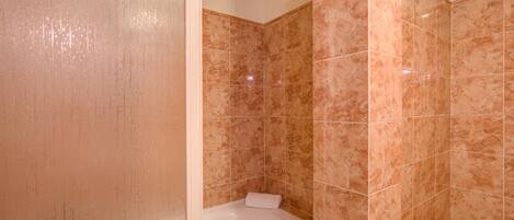 A bathroom with a white bathtub, beige tiles, and a visible shower area.