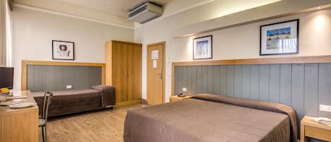 Habitación de hotel con una cama grande, una cama más pequeña, un escritorio y una silla. Hay cuadros en la pared y un equipo de aire acondicionado en el techo.