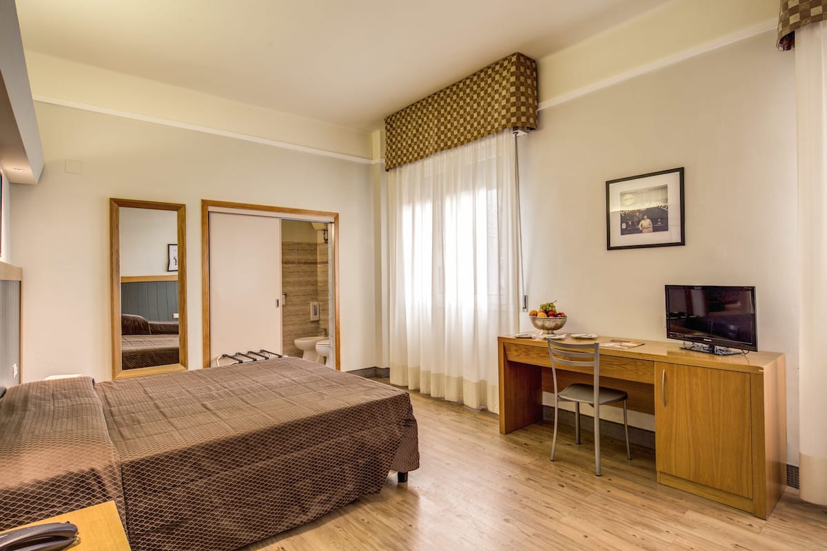Hotellihuone, jossa on sänky, työpöytä, tuoli, televisio ja kylpyhuone, joka näkyy avoimesta ovesta.