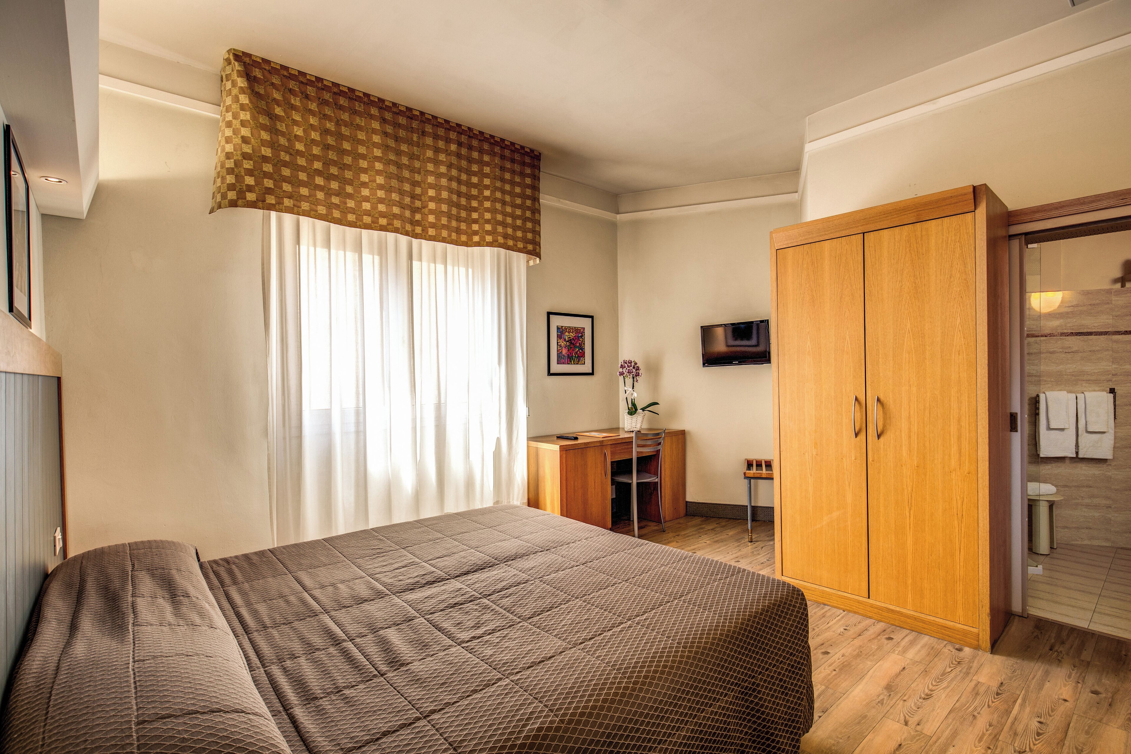 A hotel room with a bed, a desk, a wardrobe, and a television.