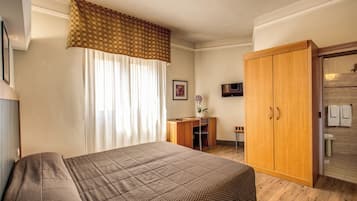 Una habitación de hotel con cama, escritorio, armario y televisor.