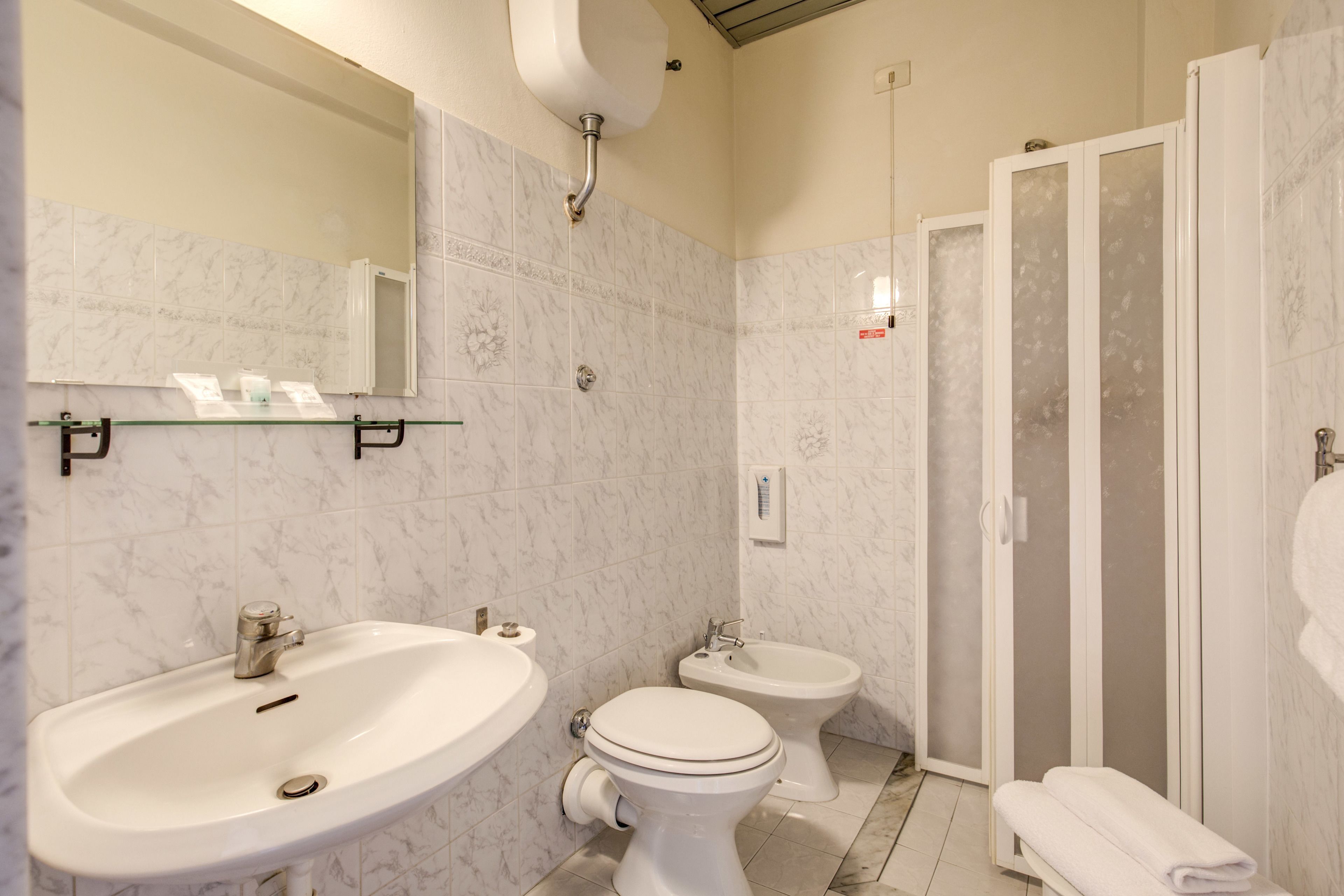 A bathroom with a sink, toilet, bidet, and a glass-enclosed shower.