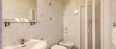 A bathroom with a sink, toilet, bidet, and a glass-enclosed shower.