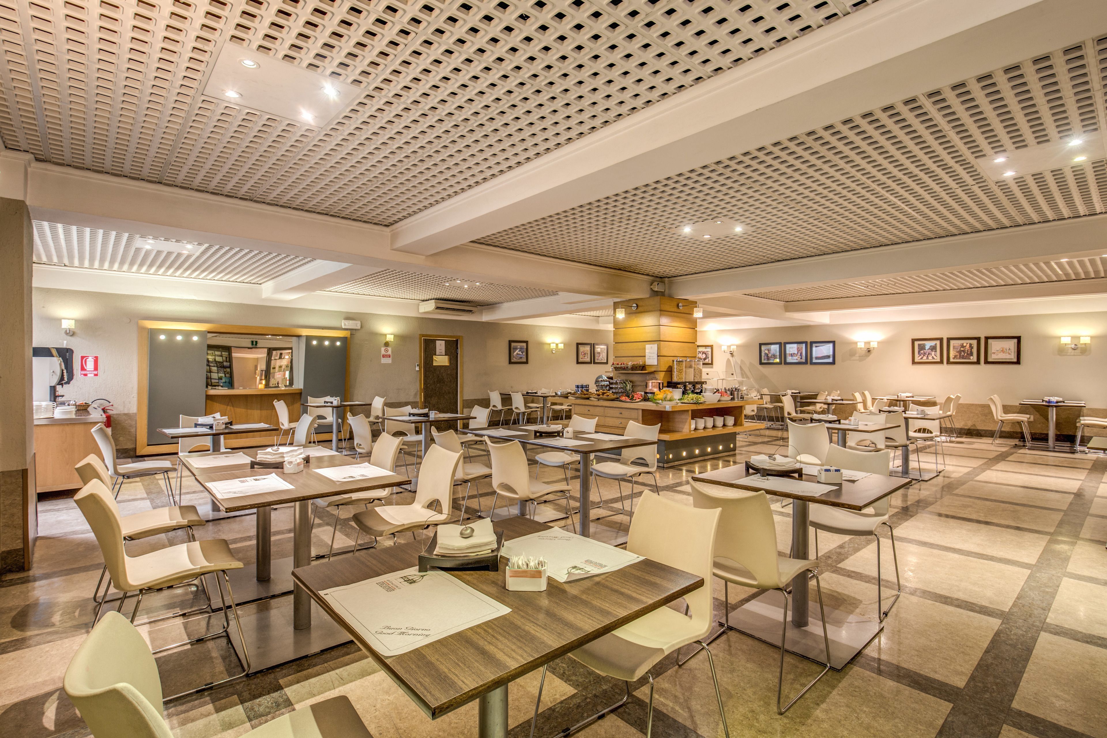 A spacious dining area with multiple tables and chairs, a central counter, and a ceiling with a grid pattern.