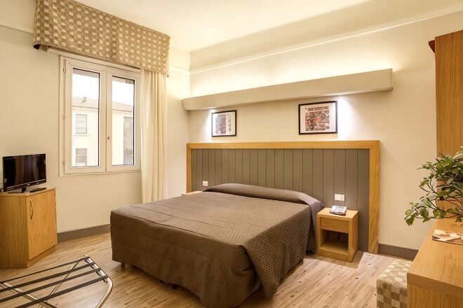 A bedroom with a bed, bedside tables, a television, and a window.