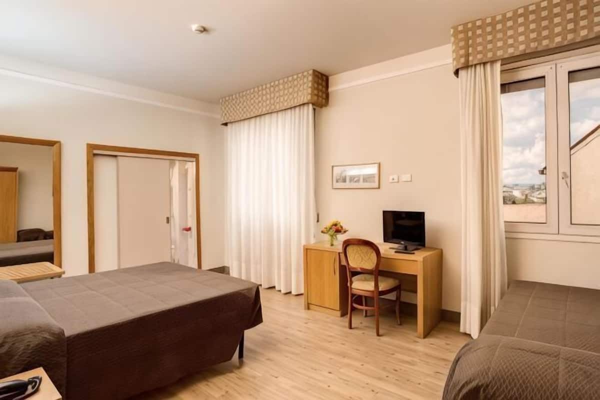 Hotellihuone, jossa on sänky, työpöytä tuolilla, televisio ja ikkuna, jossa on verhot.