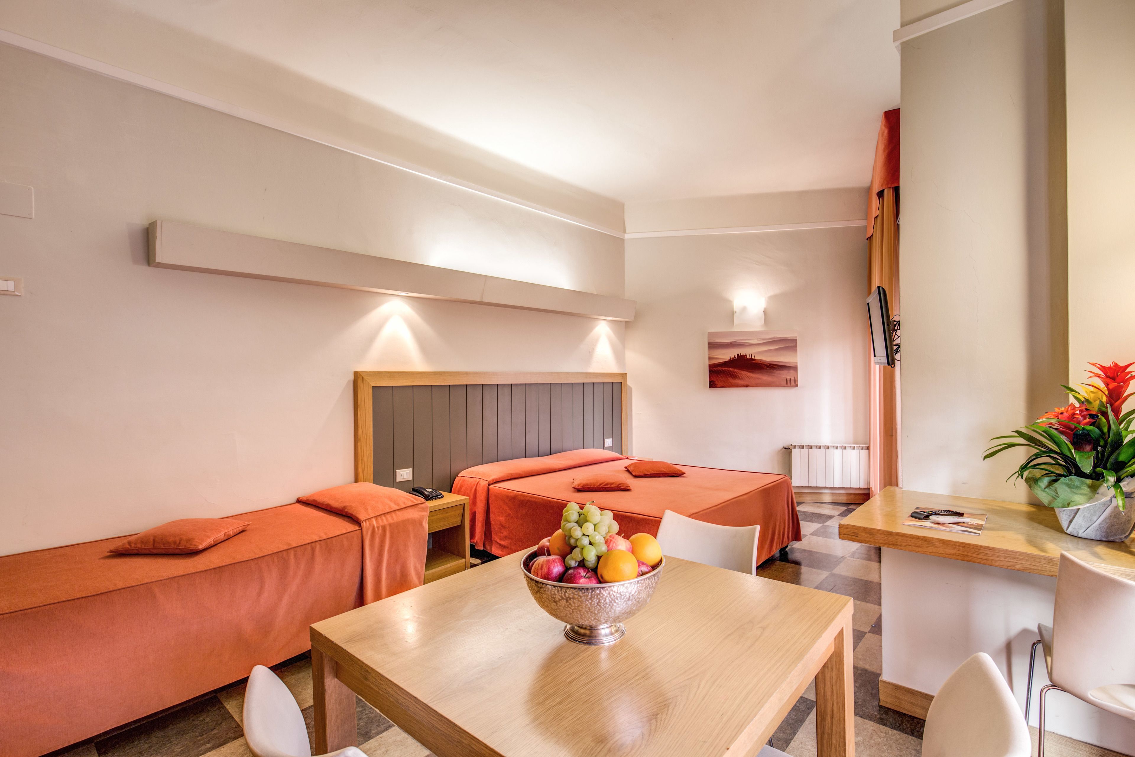 A hotel room with two single beds, a wooden table with a fruit bowl, a small dining table, and a chair.